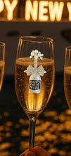 Load image into Gallery viewer, Champagne flute with a 'Happy New Year' bottle charm against a blurred festive background.