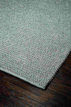 Load image into Gallery viewer, A close-up of a woven area rug corner with a textured, heathered pattern in muted sage green and dusty pink, shown on a dark wood floor.