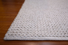 Load image into Gallery viewer, Close-up of a textured off-white woven rug corner laid on a dark brown wooden floor.
