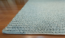 Load image into Gallery viewer, A close-up of a textured, woven area rug in a light blue-gray color, shown folded over on a polished wooden floor.
